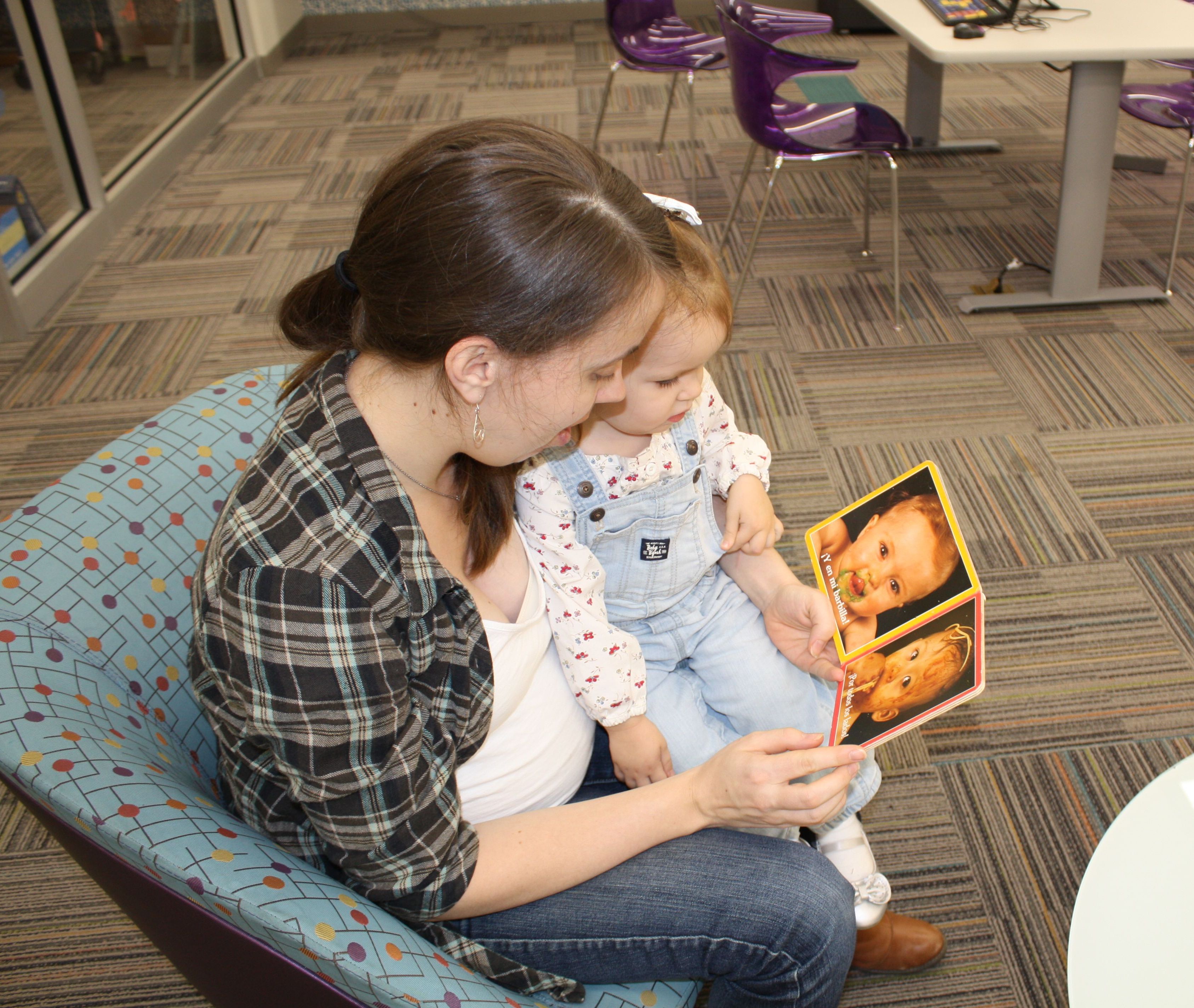 Caregiver and child sit at the library and read a book together.