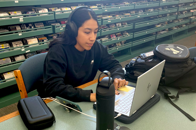 Young woman works on a laptop at the library wearing headphones