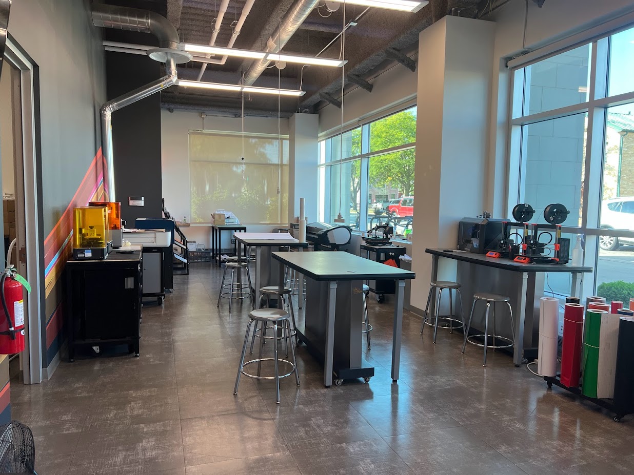 Makerspace with tall tables and stools, rolls of colorful vinyl, tools, and equipment around the perimeter of the room.
