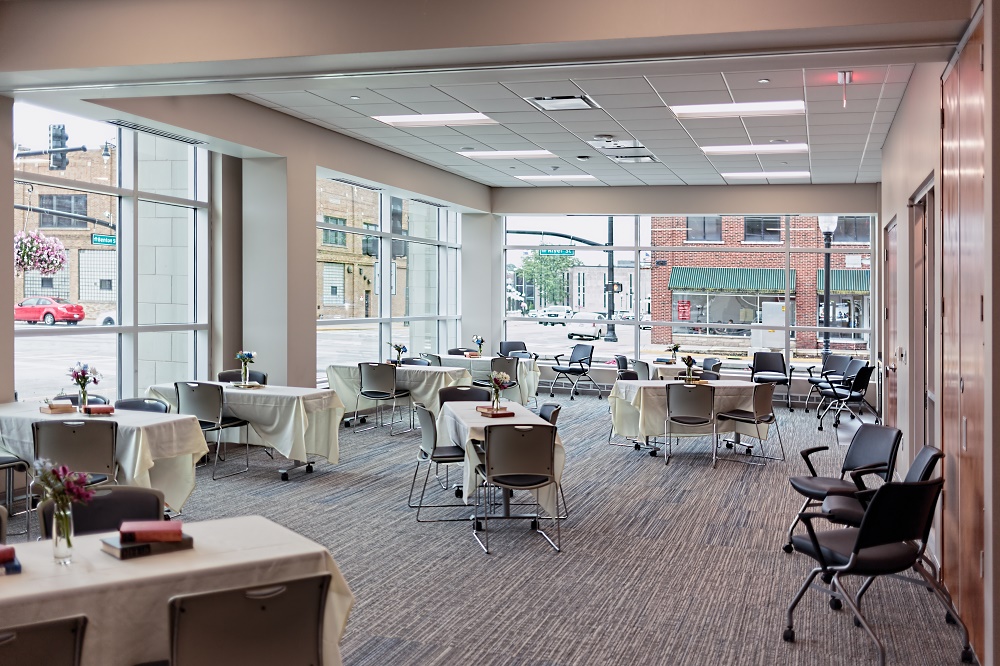Large room with glass windows set up with linen covered tables and chairs.