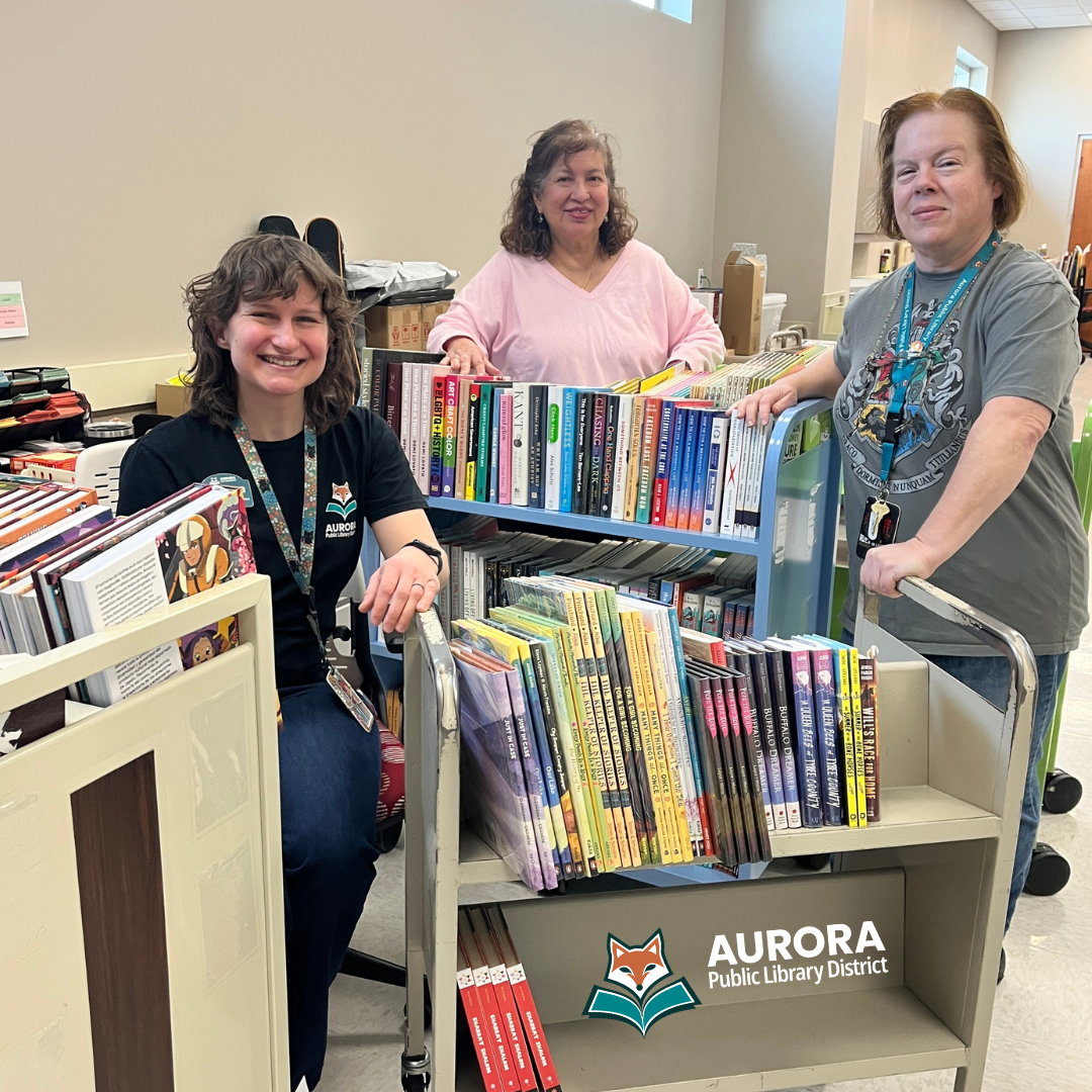 Three staff members pose with carts of library books.