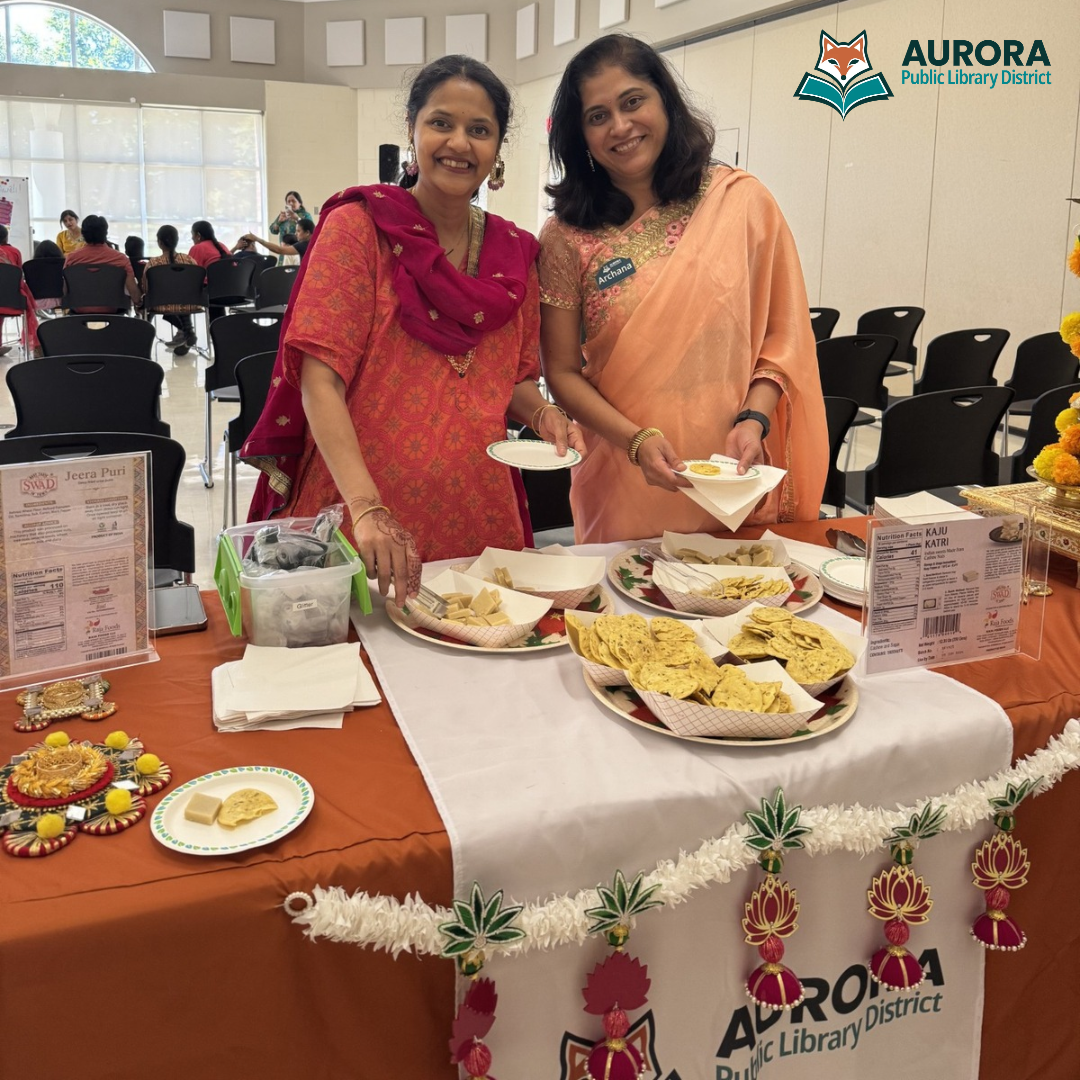 Staff members wearing traditional Indian attire smile for a photo while they prepare food during a Diwali program.