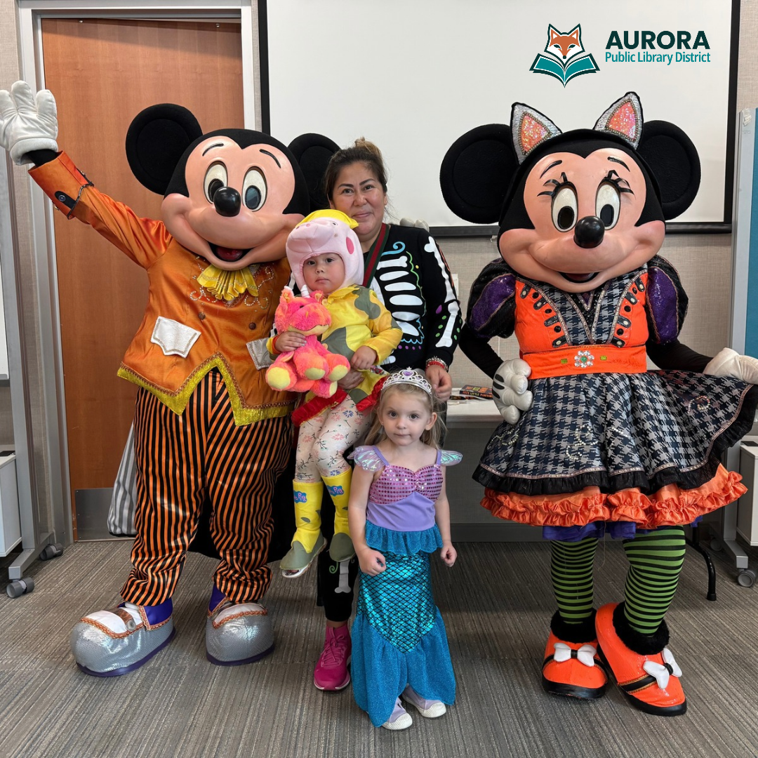 Caregiver and children dressed in Halloween costumes pose with Halloween themed character actors during a library program.