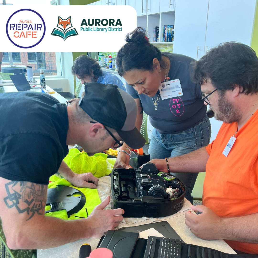 Three volunteers work on a robot vacuum during a library program.
