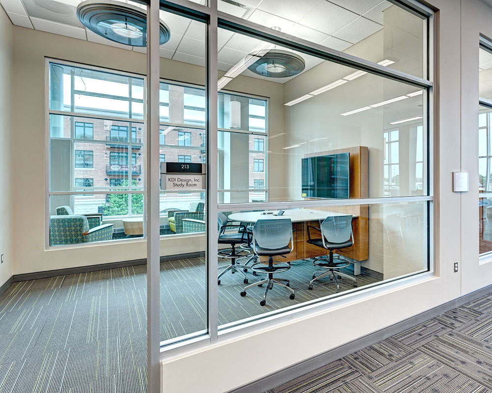 Windowed room in the library with a table, 4 chairs, and a screen mounted to the wall.